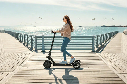 Foldable electric scooter being ridden by woman on wooden seaside pier with ocean backdrop